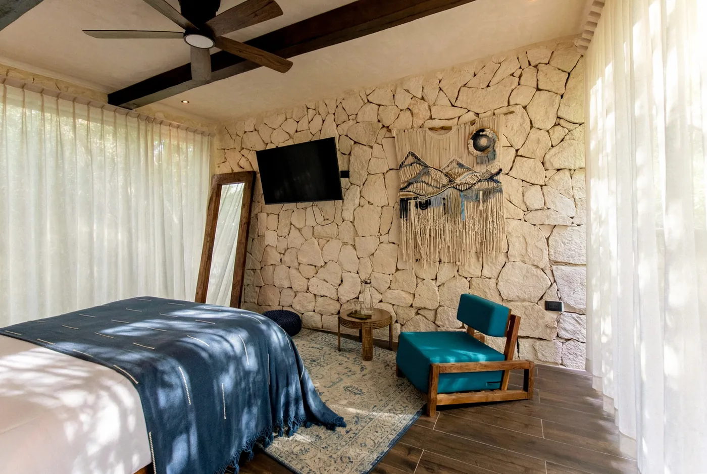 Private queen room at Kaaba Luum with a stone wall, jungle-view windows, and a teal reading chair